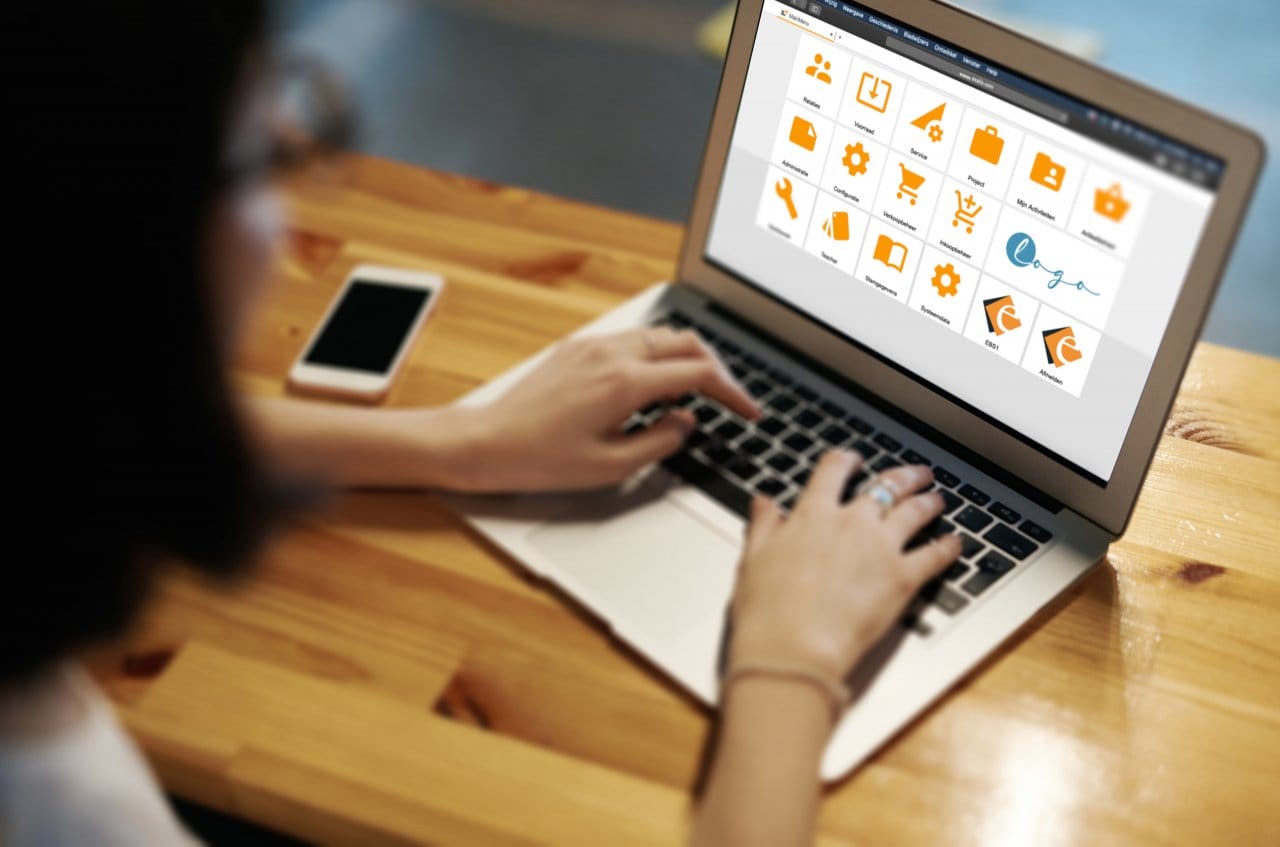 Vrouw werkt op een laptop met het tegelmenu van Exalio Business Solution, met een smartphone ernaast