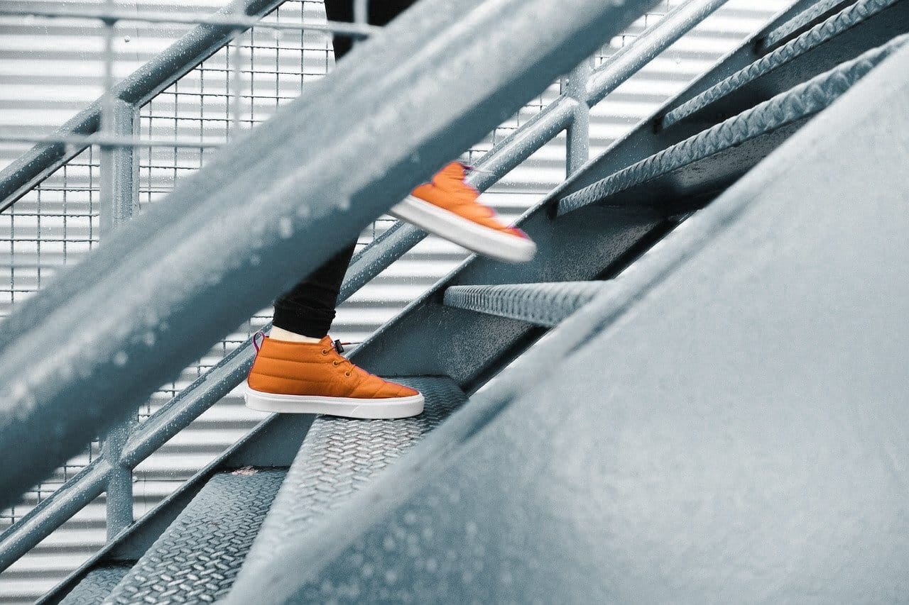 Persoon in oranje sneakers loopt een stalen trap op
